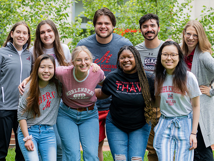 A group of college students and faculty smile and pose for a photograph outdoors.