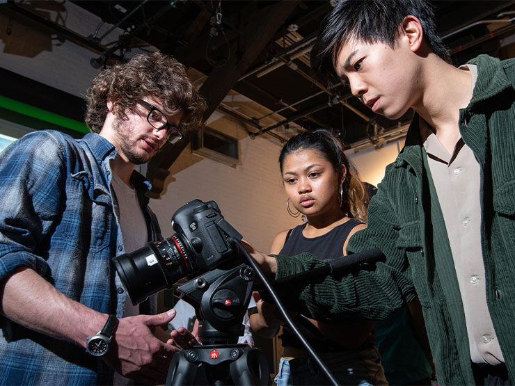 A trio of students gather around camera equipment in a studio setting.