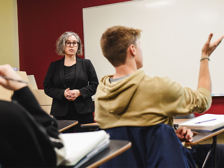 An instructor dressed in black listens as a seated student speaks.