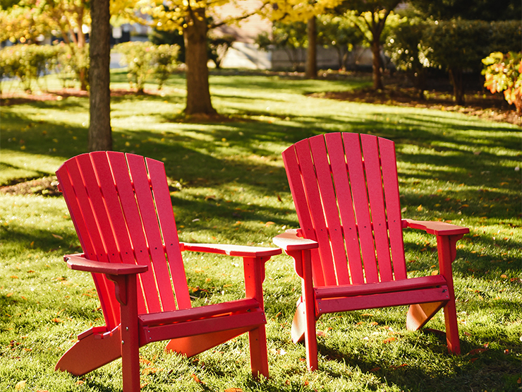 Two red adirondack chairs sit in the grass on a sunny day.