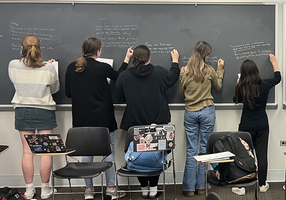 Muhlenberg College students participating in writing on blackboard in classroom setting.