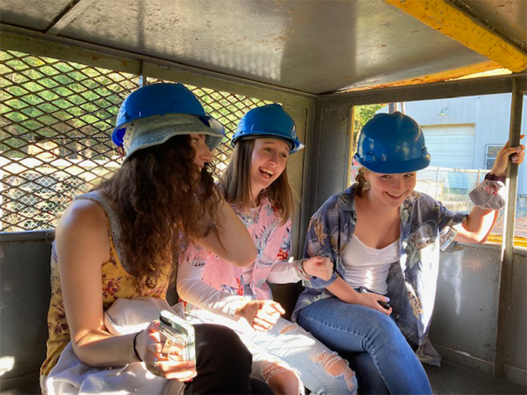 A trio of students wearing hard hats laugh together during a trip in a coal elevator.