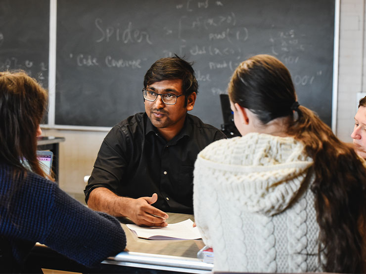 A pair of students face an instructor for a discussion in a classroom.