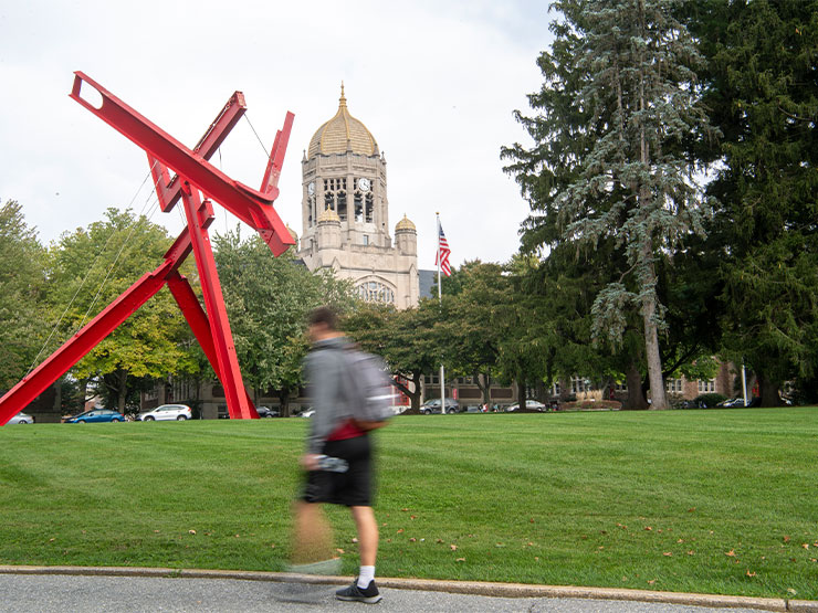 The blurry figure of a student with a backpack crosses in front of the red modern sculpture Victors Lament on the campus of Muhlenberg College.