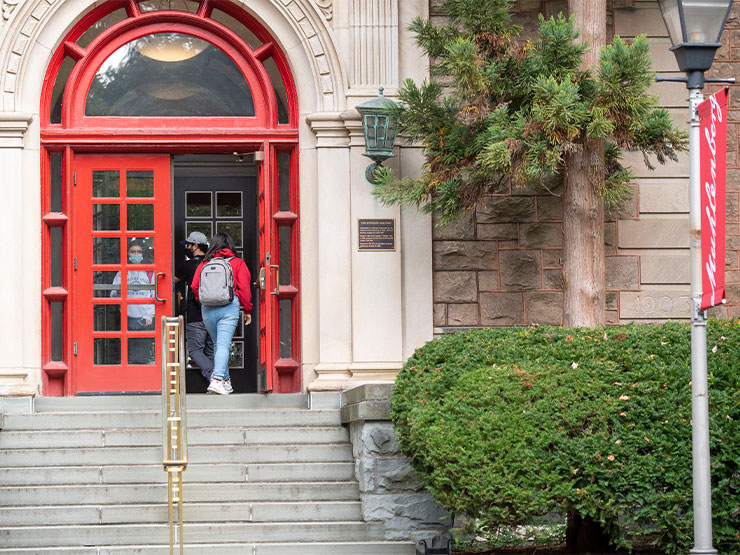 A student walks into the red doors of a stone building on the campus of Muhlenberg College.
