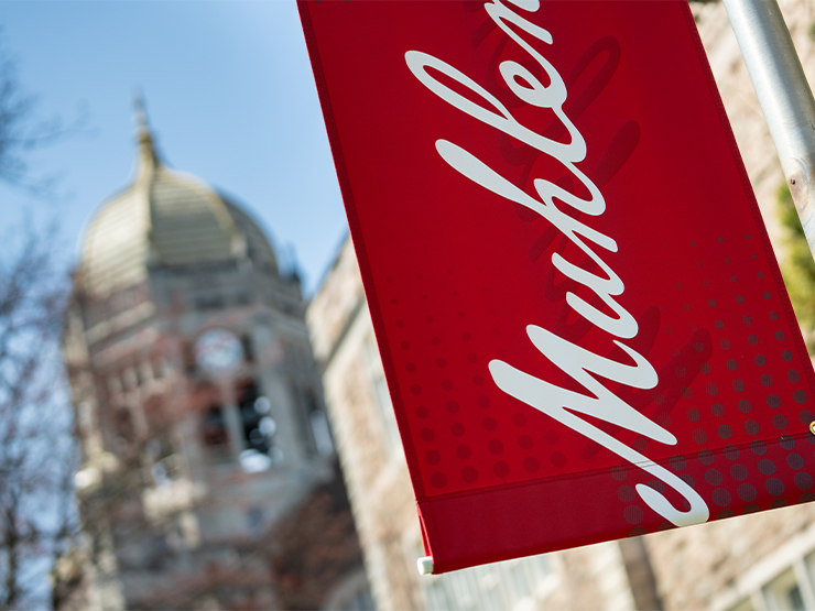 Part of a red Muhlenberg College flag is visible with Haas College Center clocktower blurry in the distance.