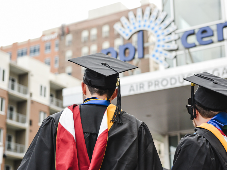A recent graduate stands with his back to the camera while signage for the 
