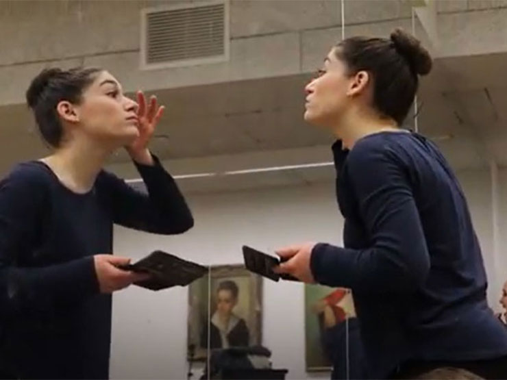A dancer applies makeup in a mirror at a studio where others prepare before showtime.