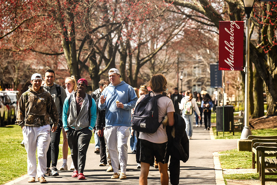 A group of college students walks down academic row on a sunny early spring day