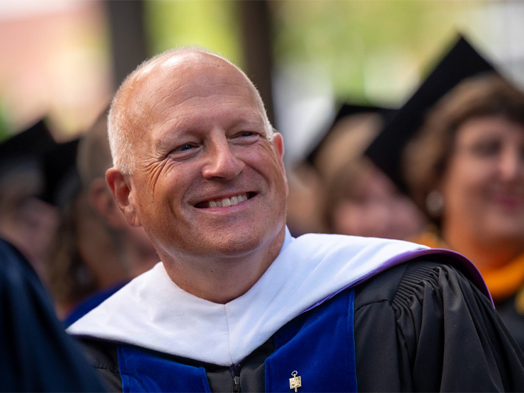 A man smiles wearing formal graduation attire.