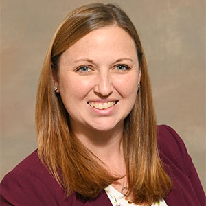 A headshot photo of a woman with shoulder-length blonde hair smiling in a maroon blazer.