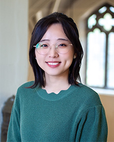 Counseling trainee smiling wearing green textured sweater and oval glasses.