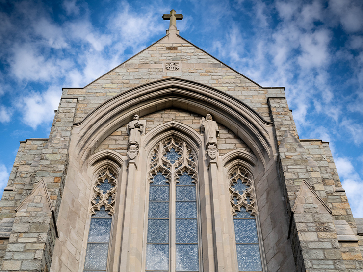 An ornate stone chapel stands against a bright blue sky studded with soft, white clouds.
