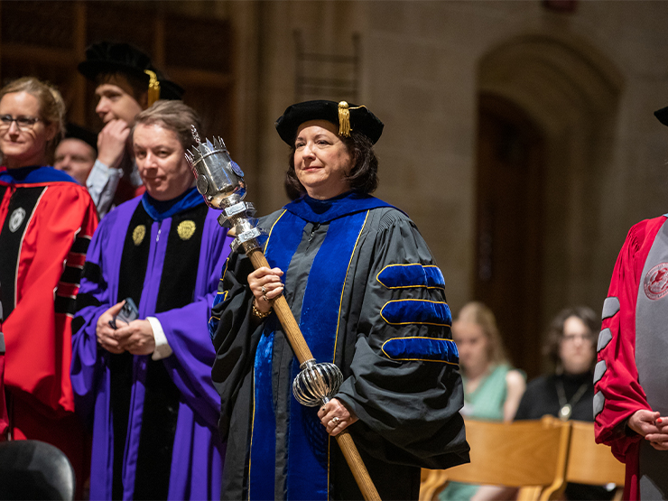 College faculty are dressed in formal regalia inside of a chapel.