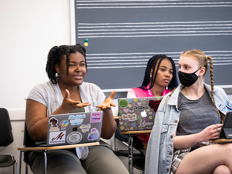 A student speaks up in a classroom as others look on.