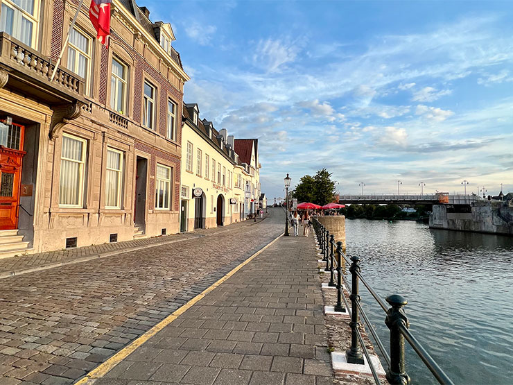 A row of old European buildings sit alongside a river under a blue sky.