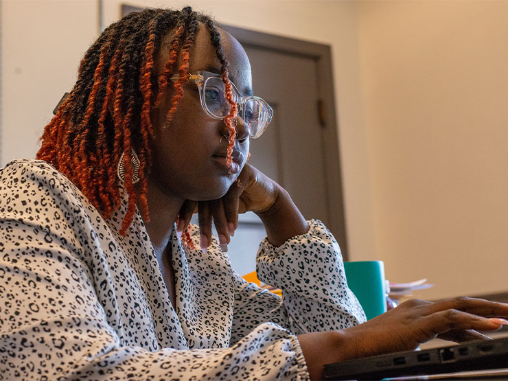 A young adult in a white patterned blouse works on a computer in an office.