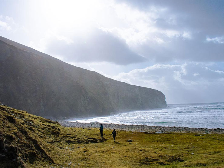 Green cliffs stand against a dramatic sea and sky in Ireland.