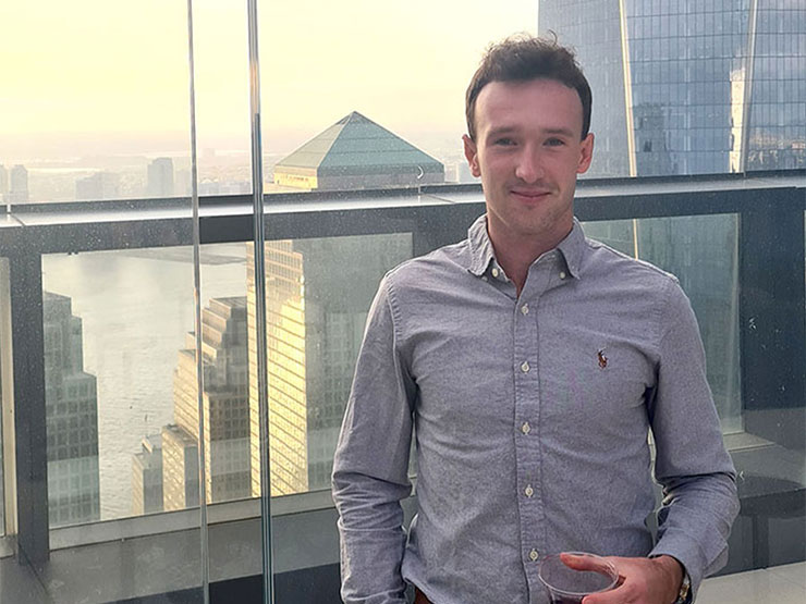 An adult in a grey collared shirt stands on a balcony overlooking a large city.