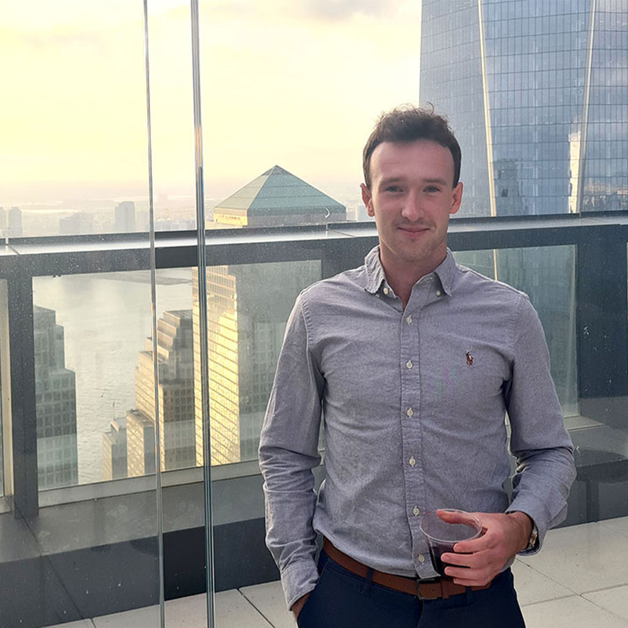 An adult in a grey collared shirt stands on a balcony overlooking a large city.