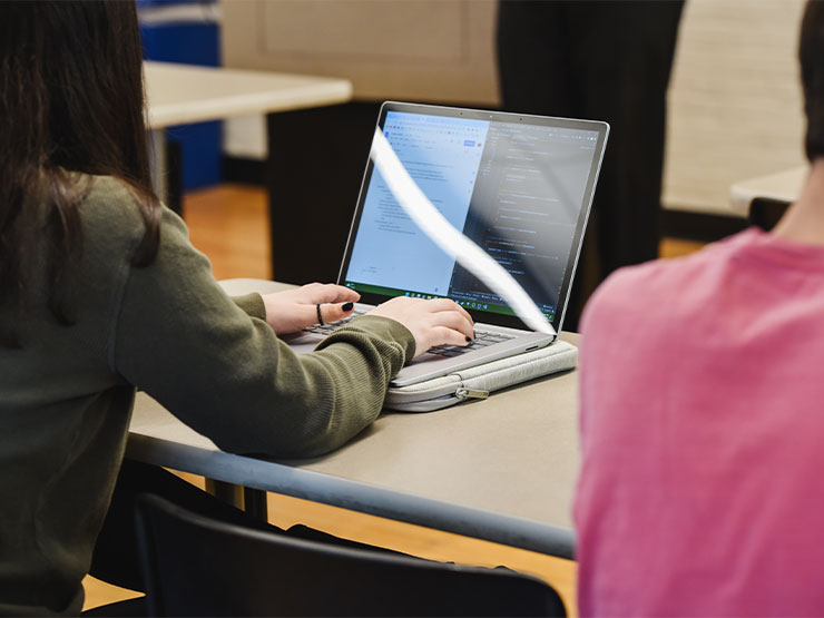 A student, whose back is to the camera, works on an open laptop.