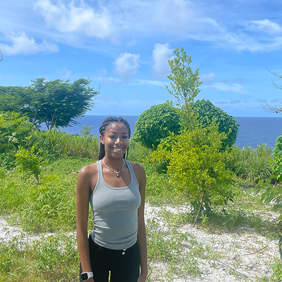 A Black woman with brown hair and athletic attire standing in a grassy field neutrally posing for a picture.