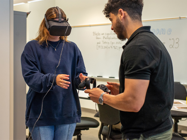A pair of students, one wearing a pair of virtual reality goggles, work on neuroscience summer research.