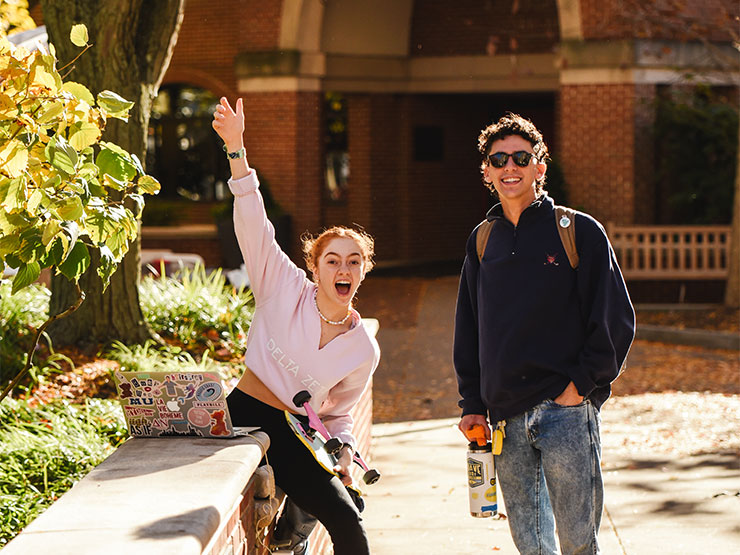 Two students on a college campus on a sunny fall day look toward the camera with open smiles.