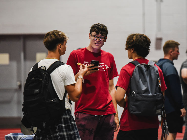 A group of three students talk together in the a gymnasium.