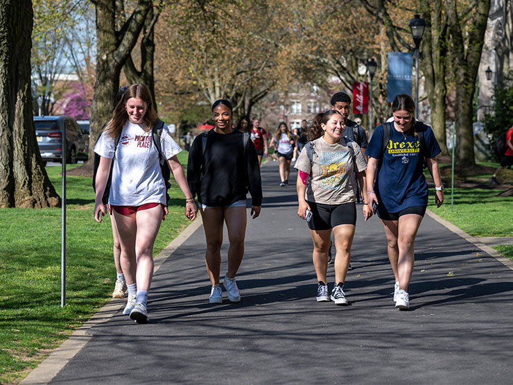 A group of four, smiling students walk down academic row in the spring at Muhlenberg College.