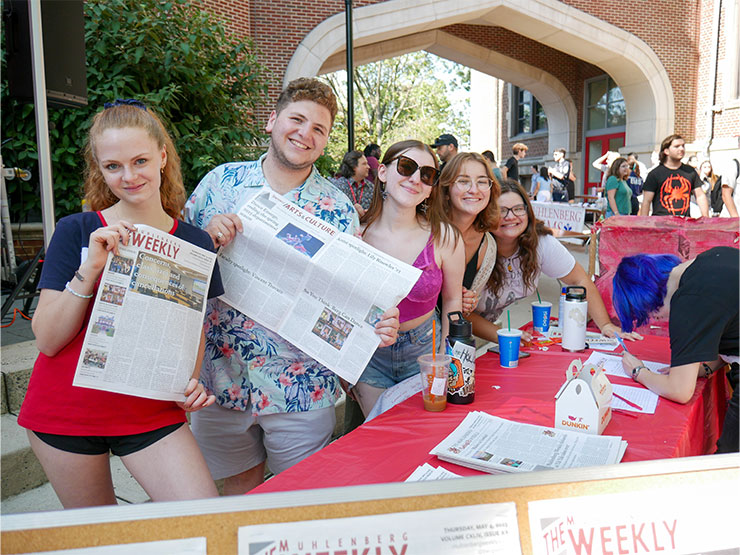 Young adults smile at the camera holding up newspapers with the masthead