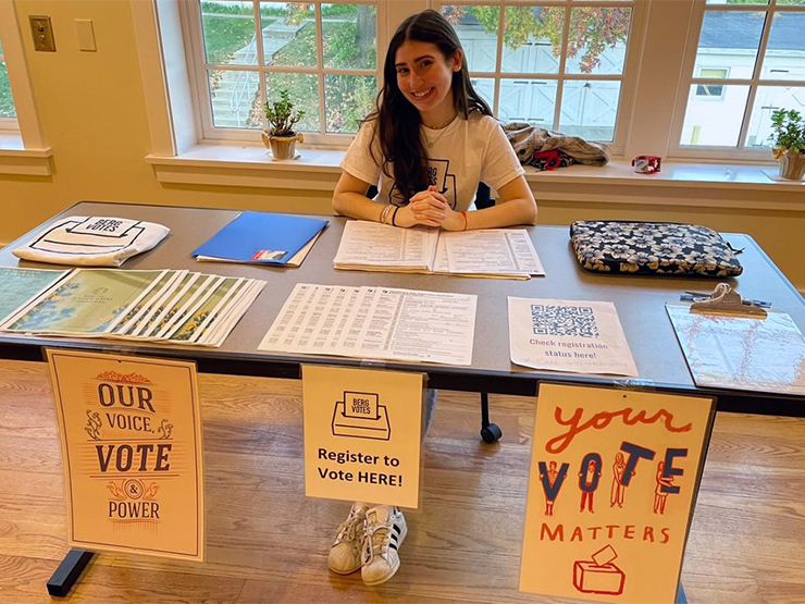 A students sits behind a table adorned with BergVotes club information and posters.