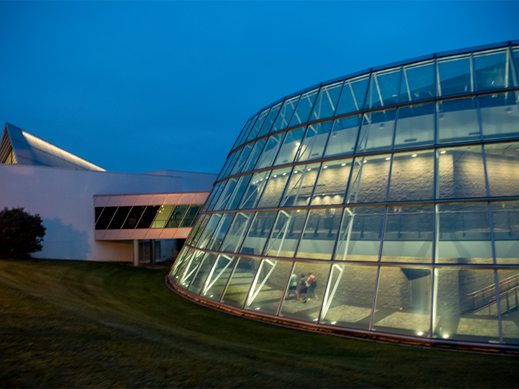 The round glass rotunda of the Baker Center for the Arts is light from within as the sky darkens.