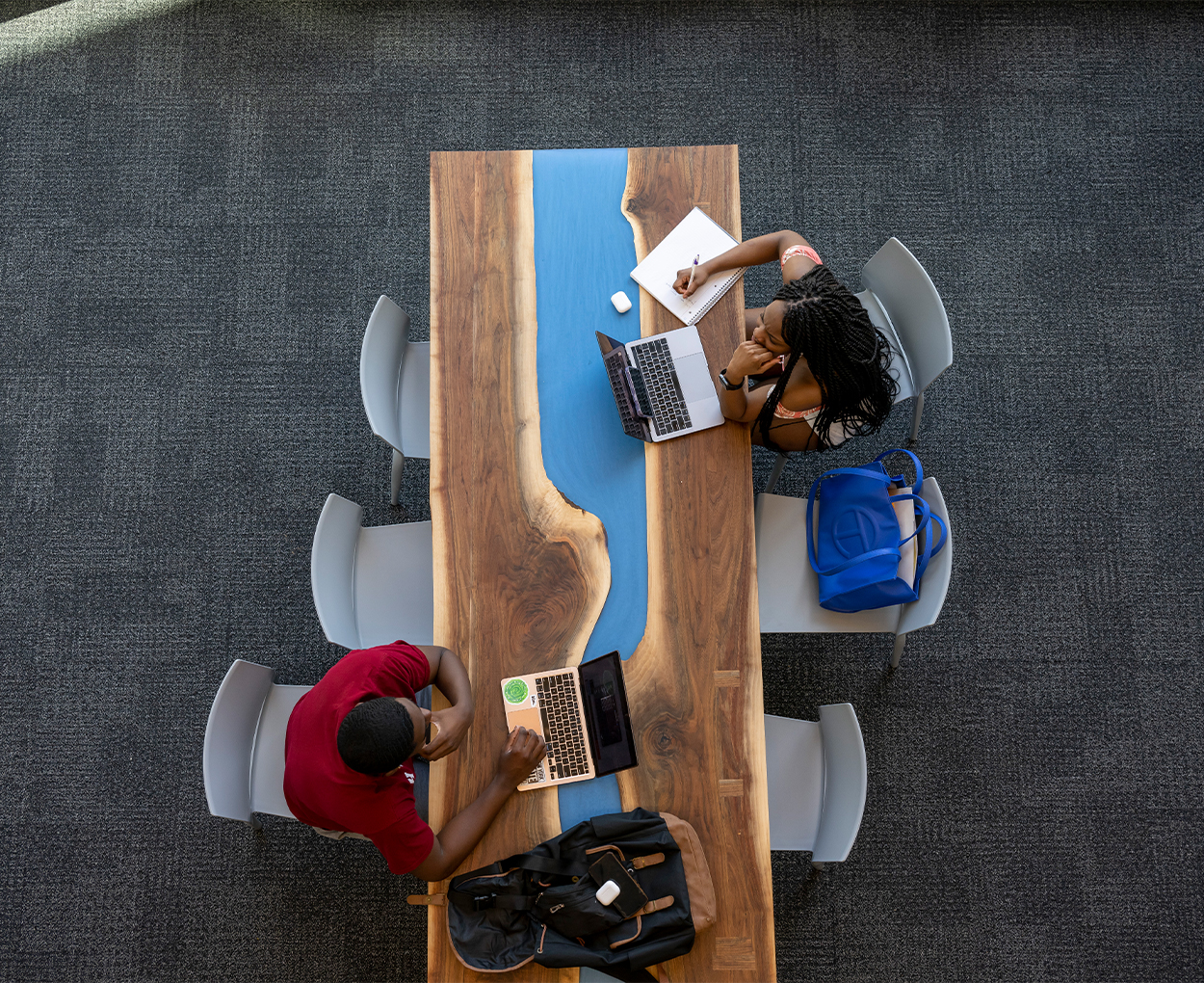 Two students sit across from one another at a wooden table, as seen from above.