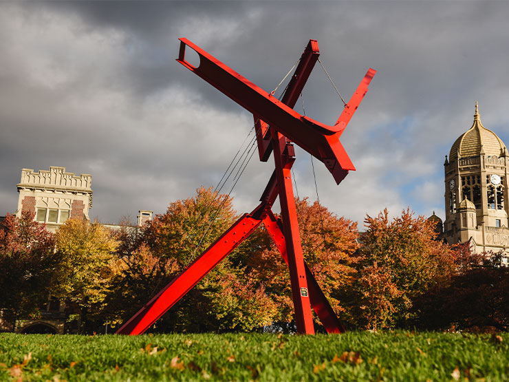 A large, red modern art sculpture stands against a dramatic sky on the Muhlenberg College campus.