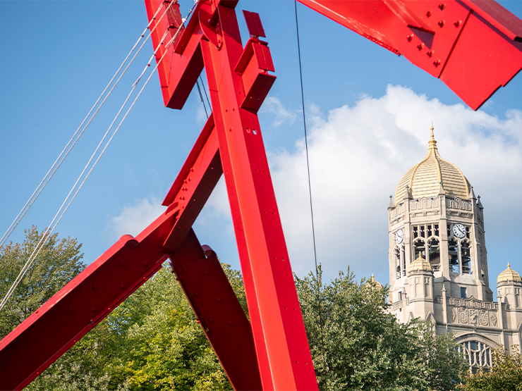 Victor's Lament, a large red modern art sculpture stands in the foreground with the bell tower of Haas College Center in the background.