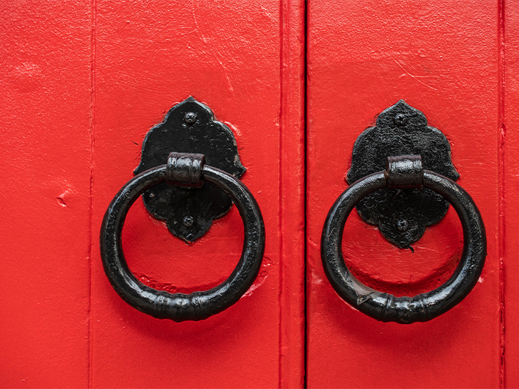 A close up of a pair of painted red doors and ornate black metal door handles.
