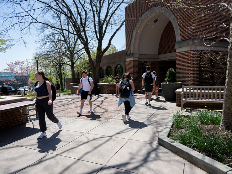 Students file in and out of a brick building, Seegers Union, on the campus of Muhlenberg College on a sunny day in early spring.