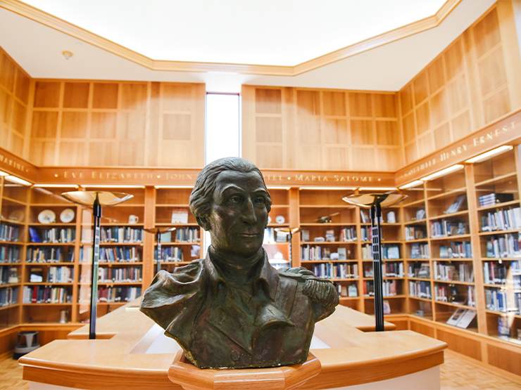 The bust of a man sits in the Trexler Library, surrounded by packed wooden bookshelves.