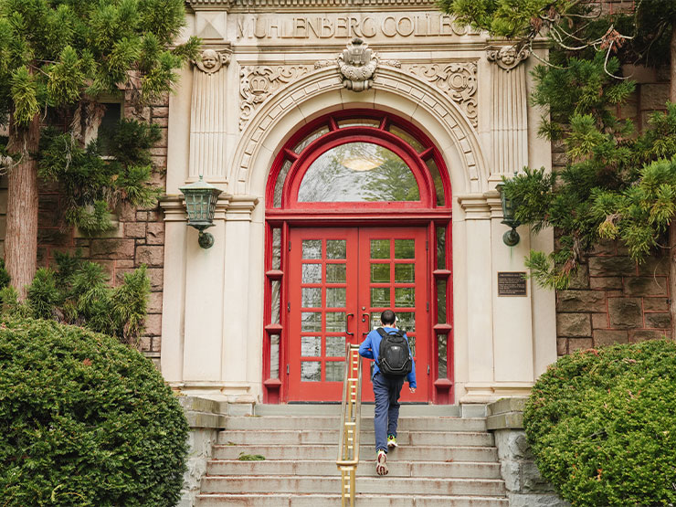 A college student walks toward a pair of red double doors on the Ettinger building at Muhlenberg College.