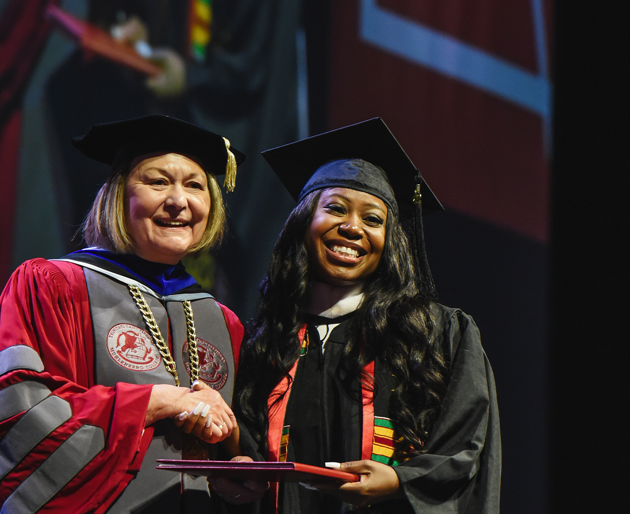 College president poses with a grad accepting their diploma.
