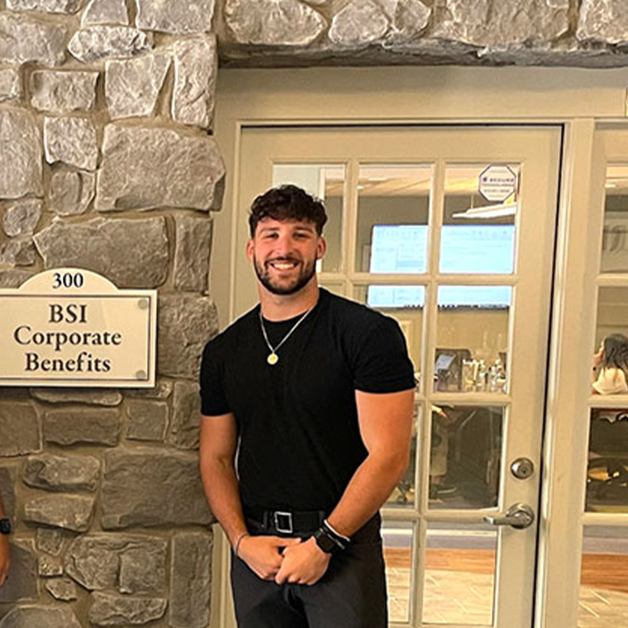 Two adults stand in front of a building with a sign that says BSI Corporate Benefits hanging on the wall between them.