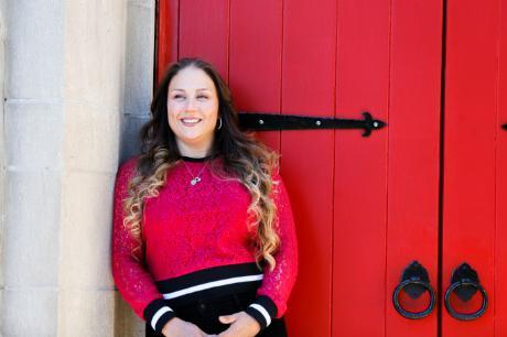 Alejandra Long standing in front of red doors leaning on wall