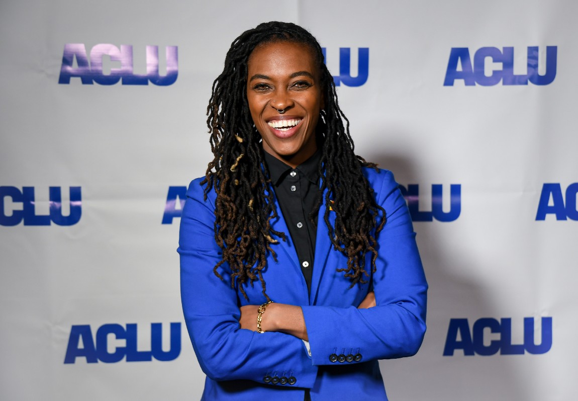 A Black person in a blue jacket smiles at the camera.