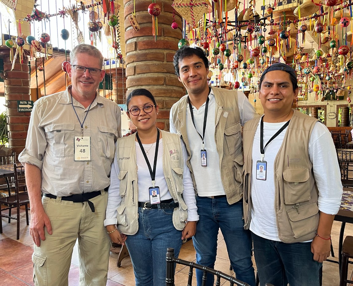 Four people stand smiling at the camera, with Mexican decor hanging from the room ceiling.