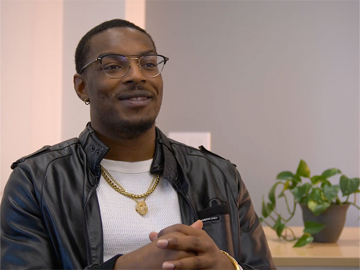 A student in a white shirt and black jackets speaks to the camera.