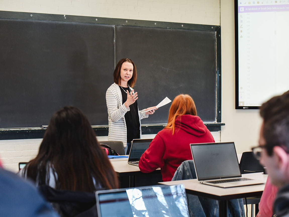 A college professor stands in front of a blackboard and speaks to students