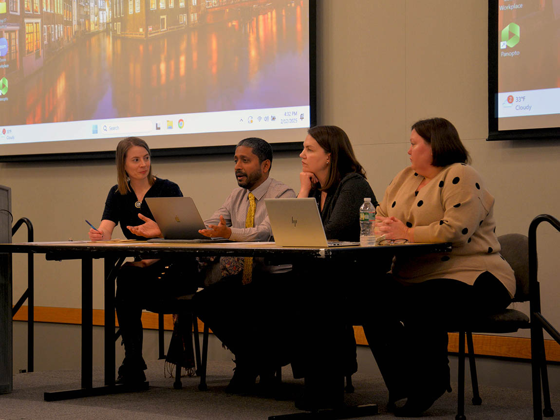 Four college faculty members sit at a table and speak on a panel