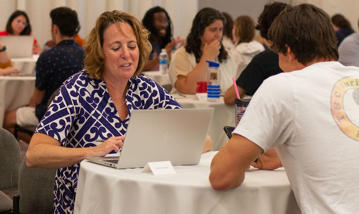 A college professor sits in front of a laptop and advises a student