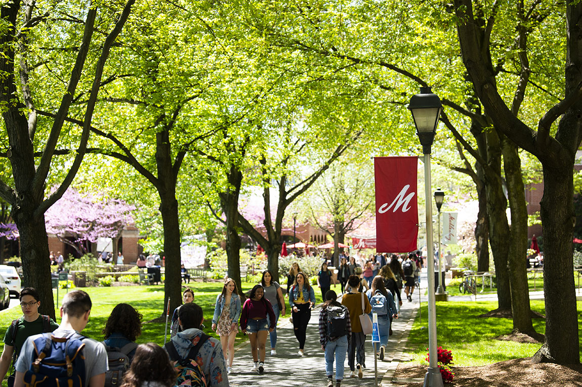 College students walk down Academic Row in the spring under some trees with green leaves and others with pink flowerrs